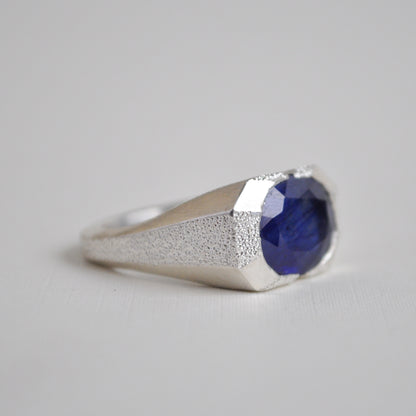 Silver ring with a blue gemstone on a light gray background
