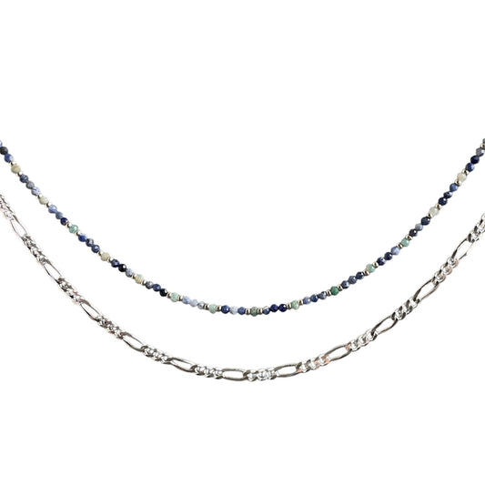 Layering necklace on a white background, one with a blue beaded chain and the other with a figaro chain.