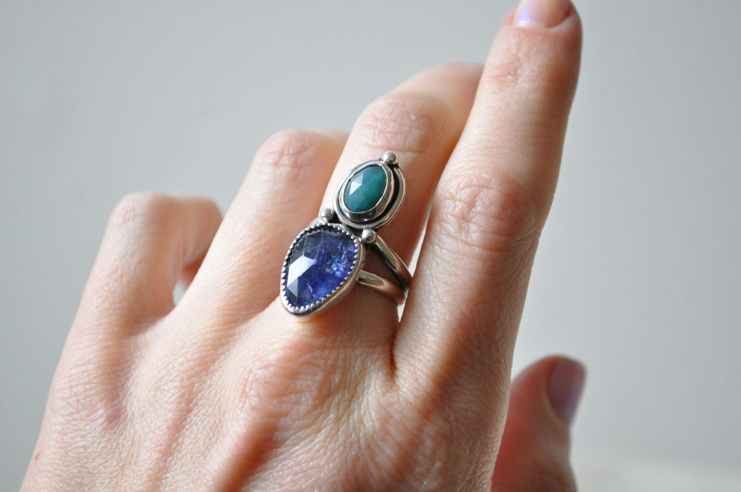 Silver ring with blue and green gemstones on a hand against a neutral background