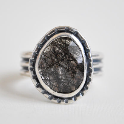 Silver ring with a dark stone on a light gray background