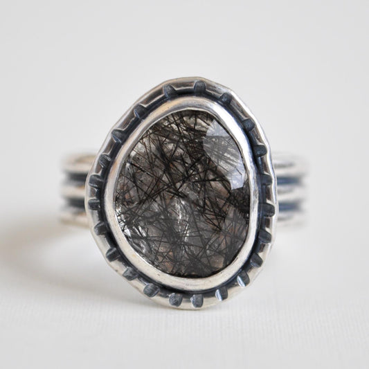 Silver ring with a dark stone on a light gray background