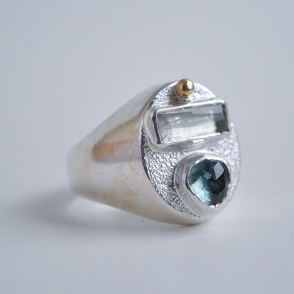 Silver ring with a blue gemstone and gold accents on a light gray background