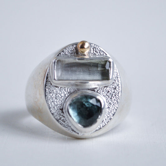 Silver ring with blue gemstone and gold accent on a light gray background