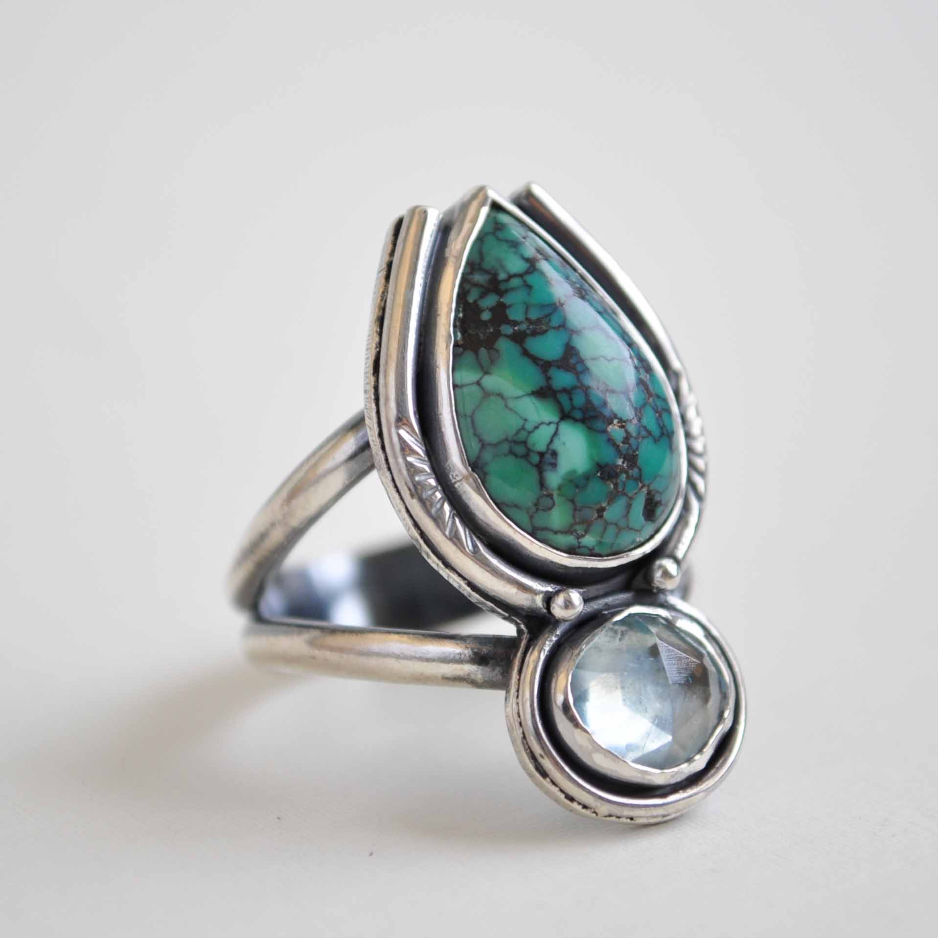 Silver ring with turquoise and clear gemstones on a light background