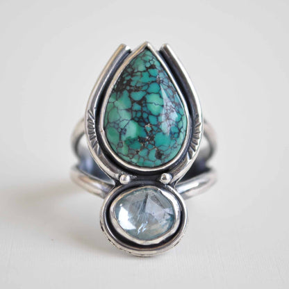 Silver ring with turquoise and clear blue gemstones on a light background