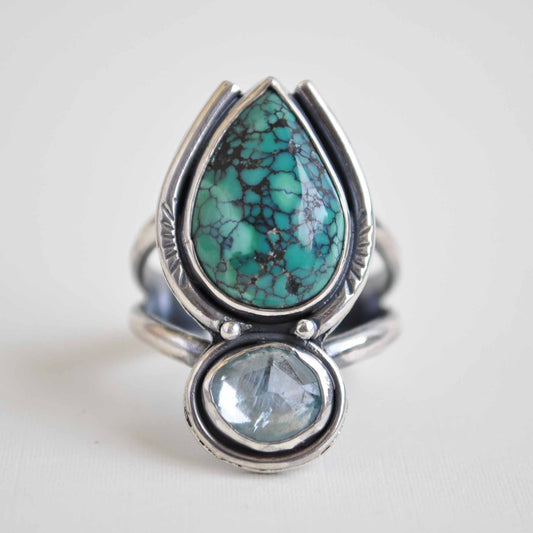 Silver ring with turquoise and clear blue gemstones on a light background