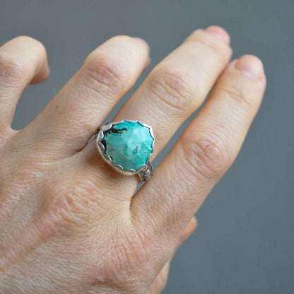 Turquoise ring on a finger against a gray background